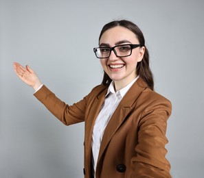 Photo of Happy businesswoman welcoming clients or partners by video call on grey background, view through camera