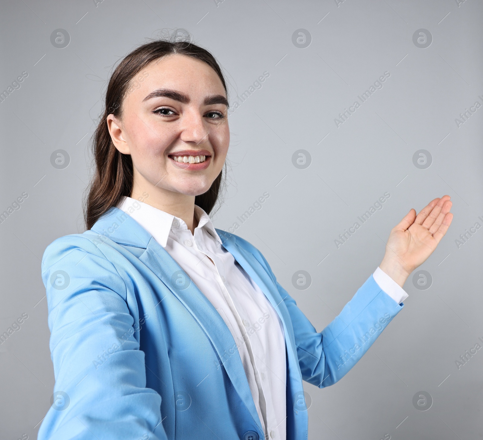 Photo of Happy businesswoman taking selfie and welcoming clients or partners on grey background