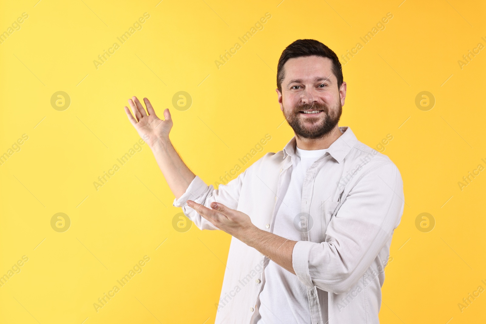 Photo of Happy man welcoming friends or guests on yellow background. Space for text