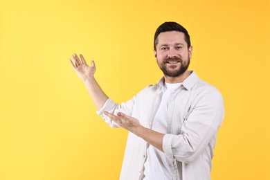 Photo of Happy man welcoming friends or guests on yellow background. Space for text