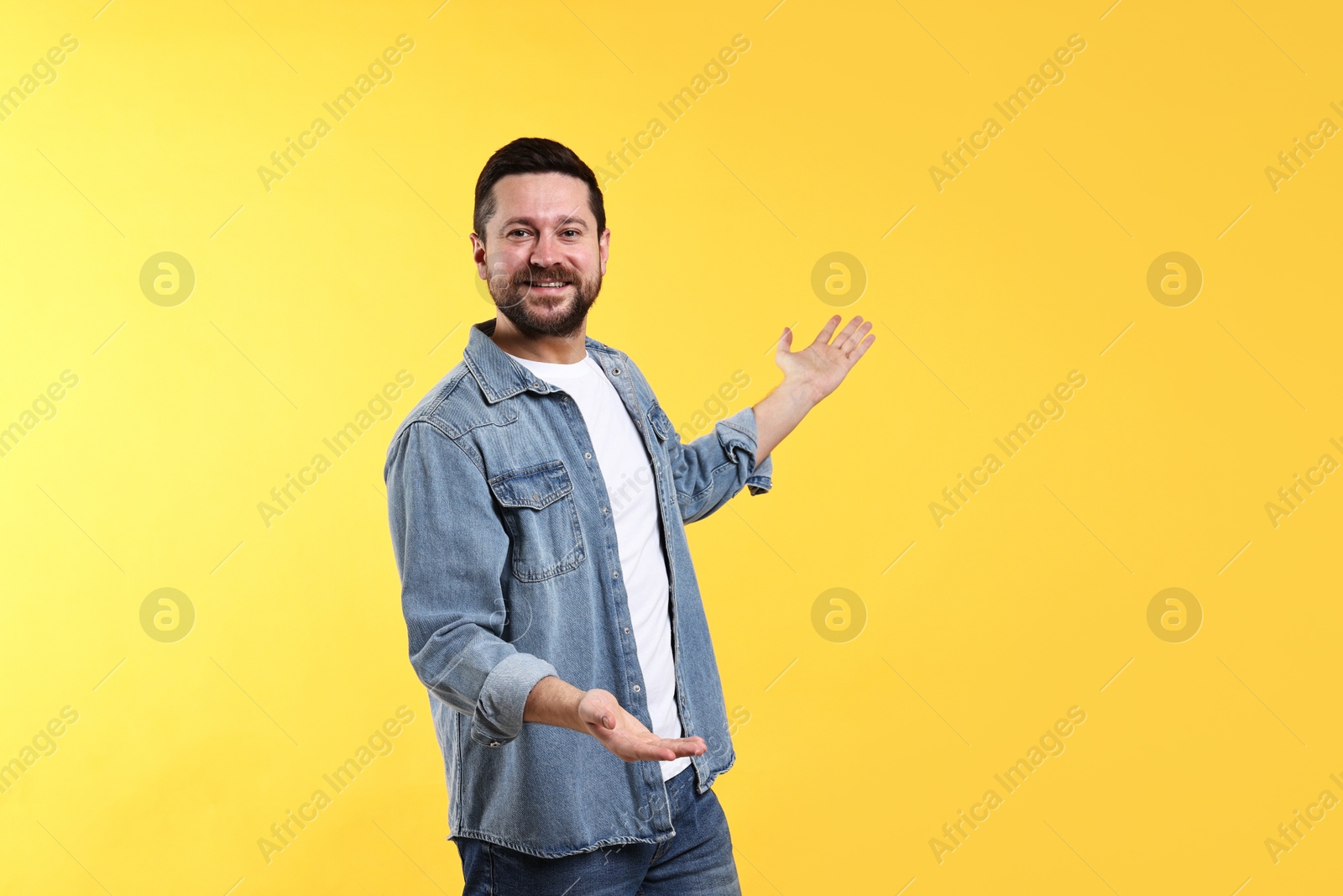 Photo of Happy man welcoming friends or guests on yellow background. Space for text