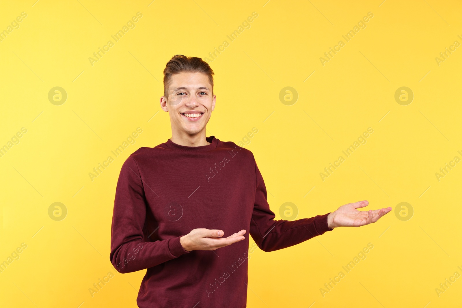 Photo of Happy man welcoming friends or guests on yellow background