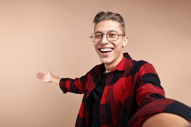 Photo of Happy man taking selfie and welcoming friends or guests on beige background. Space for text