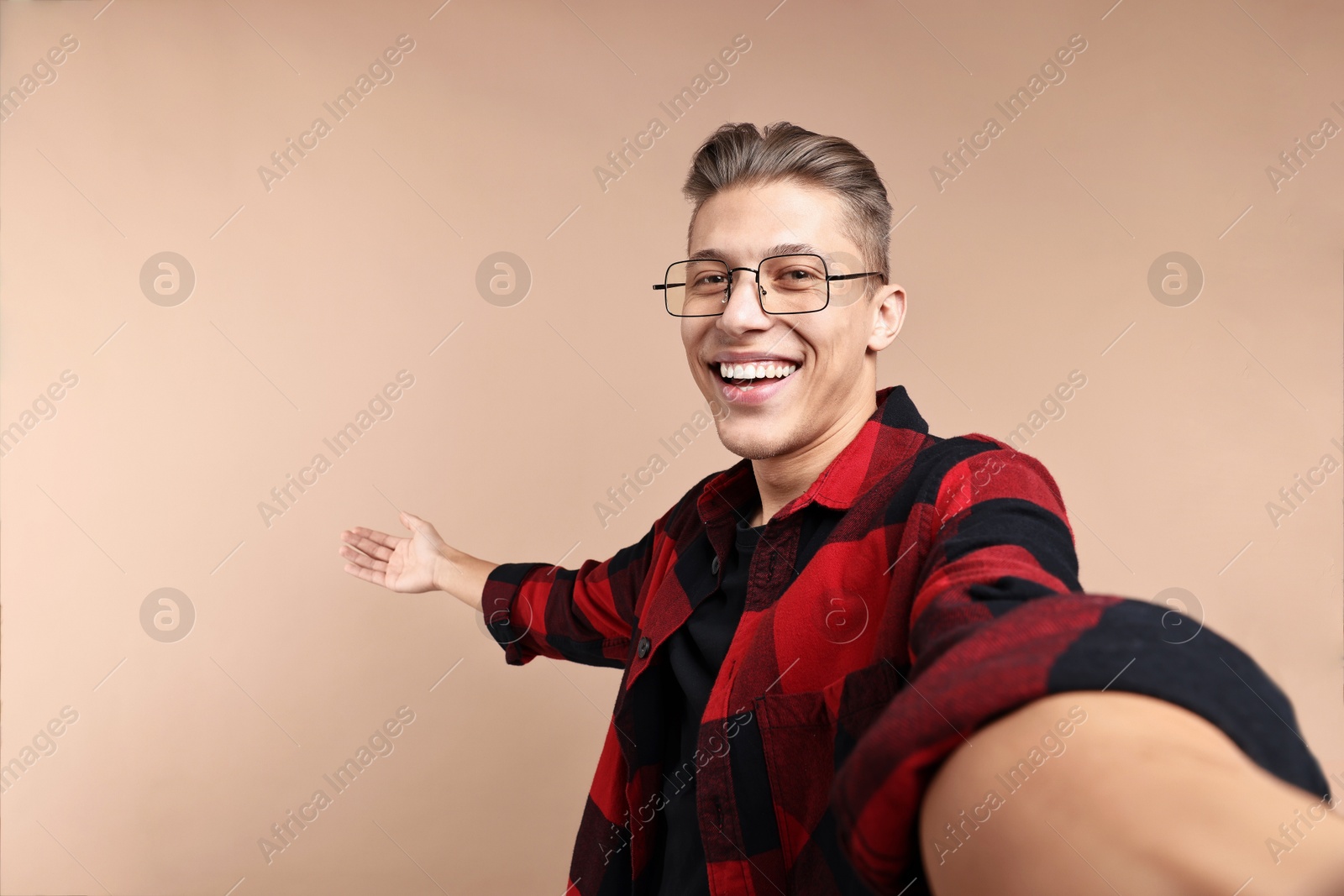 Photo of Happy man taking selfie and welcoming friends or guests on beige background. Space for text