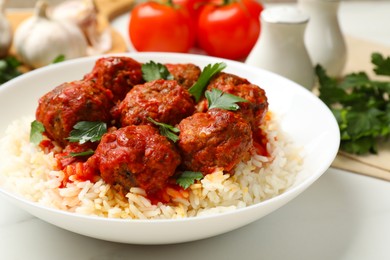 Photo of Delicious meatballs with rice, sauce and parsley on white table, closeup