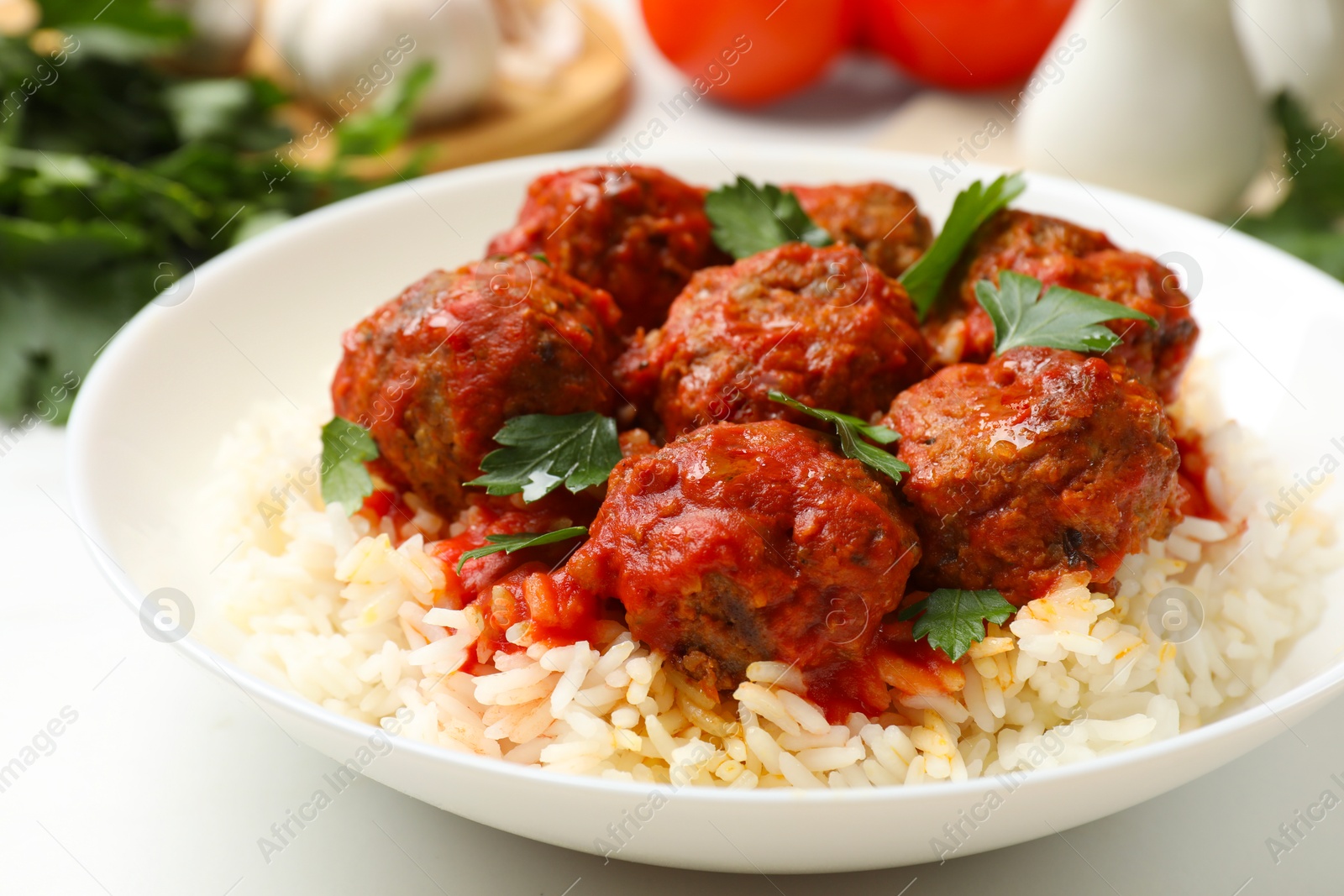 Photo of Delicious meatballs with rice, sauce and parsley on white table, closeup