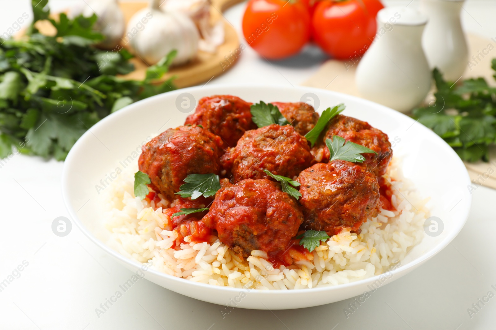 Photo of Delicious meatballs with rice, sauce and parsley on white table, closeup