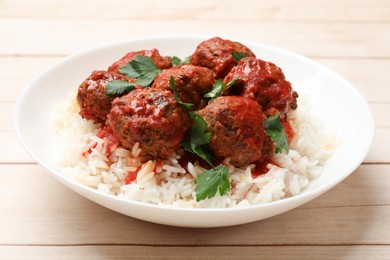 Photo of Delicious meatballs with rice, sauce and parsley on light wooden table, closeup