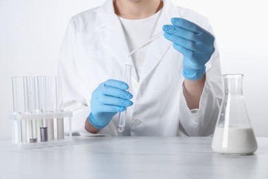 Photo of Laboratory testing. Scientist dripping liquid into test tube at table, closeup