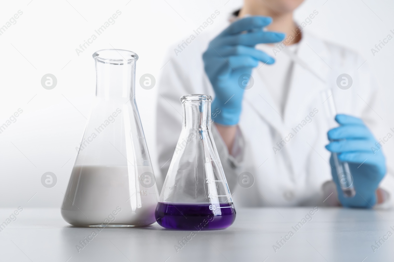 Photo of Laboratory testing. Scientist working with glassware at white marble table, focus on flasks