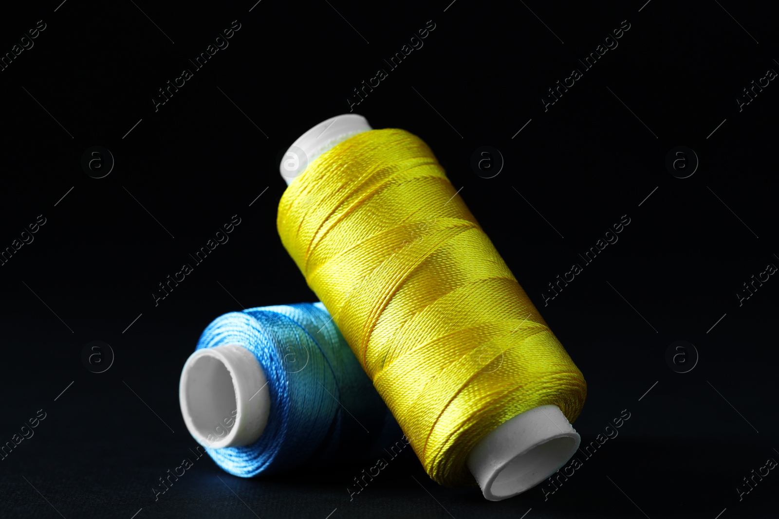 Photo of Spools of colorful sewing threads on black background, closeup