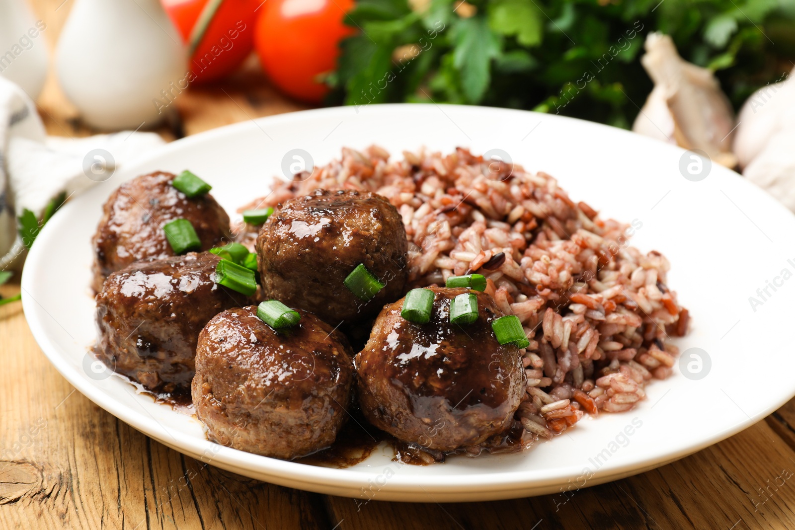 Photo of Tasty meatballs with sauce, brown rice and green onion on wooden table, closeup