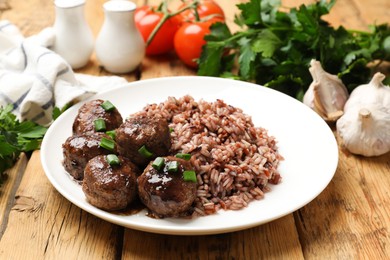 Photo of Tasty meatballs with sauce, brown rice and green onion on wooden table, closeup