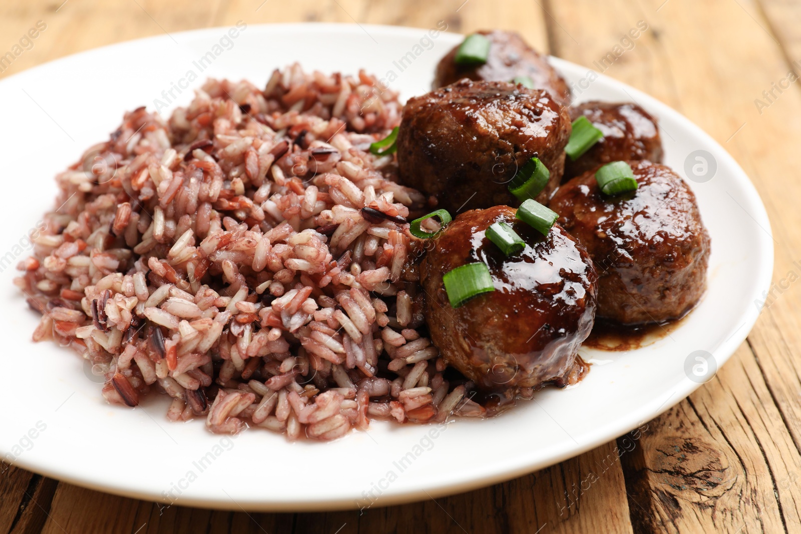 Photo of Tasty meatballs with sauce and brown rice on wooden table, closeup