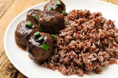 Photo of Tasty meatballs with sauce and brown rice on wooden table, closeup