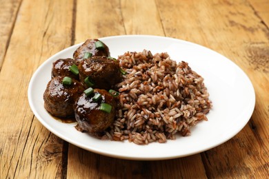 Photo of Tasty meatballs with sauce and brown rice on wooden table, closeup