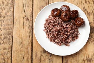 Photo of Tasty meatballs with sauce and brown rice on wooden table, top view. Space for text