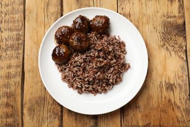 Photo of Tasty meatballs with sauce and brown rice on wooden table, top view