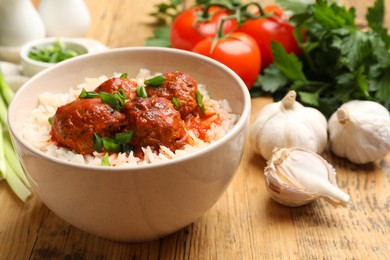 Photo of Tasty meatballs with sauce, rice and products on wooden table, closeup