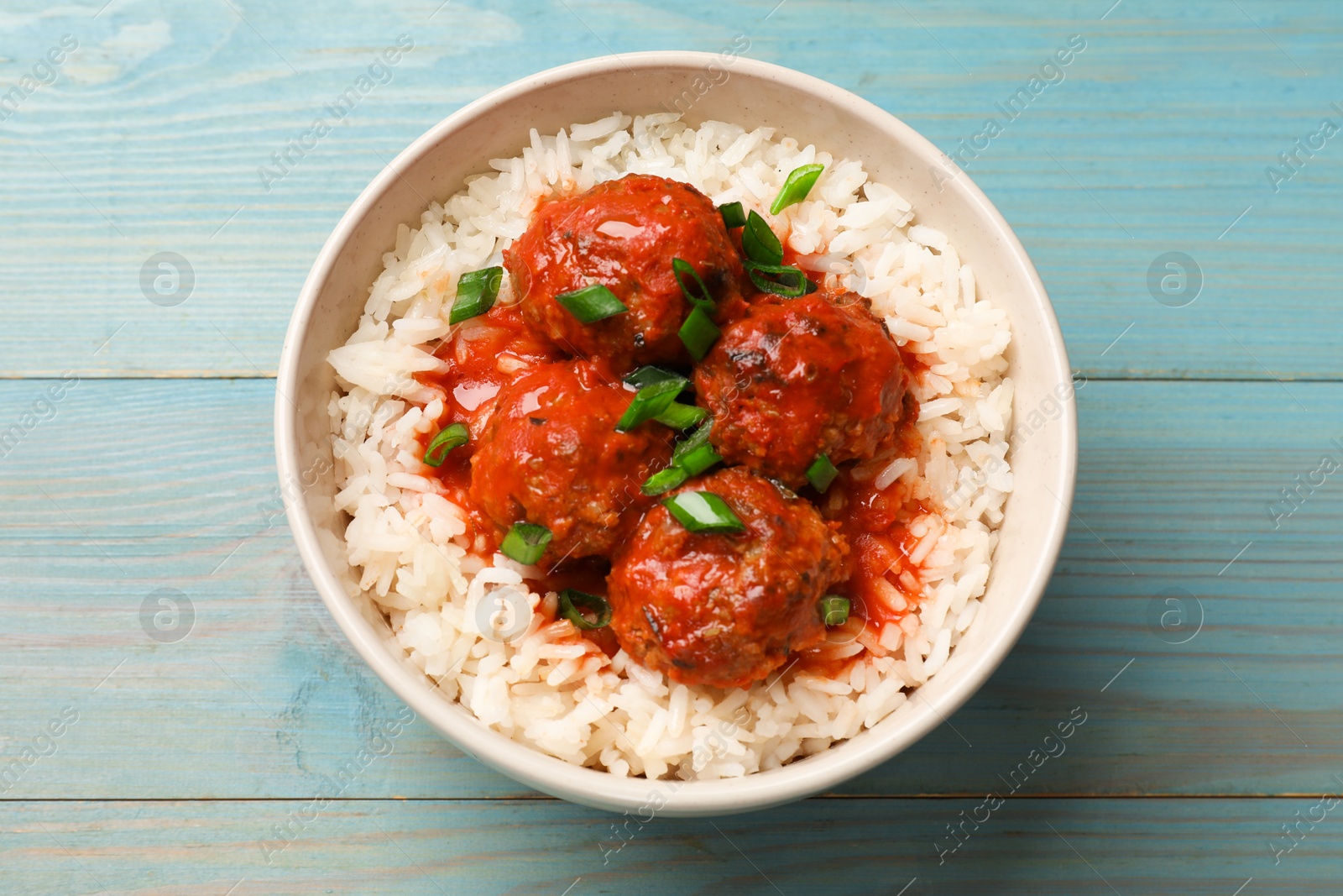 Photo of Tasty meatballs with sauce and rice on light blue wooden table, top view