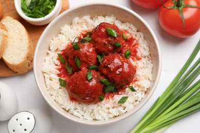 Photo of Tasty meatballs with sauce, rice and products on white tiled table, flat lay