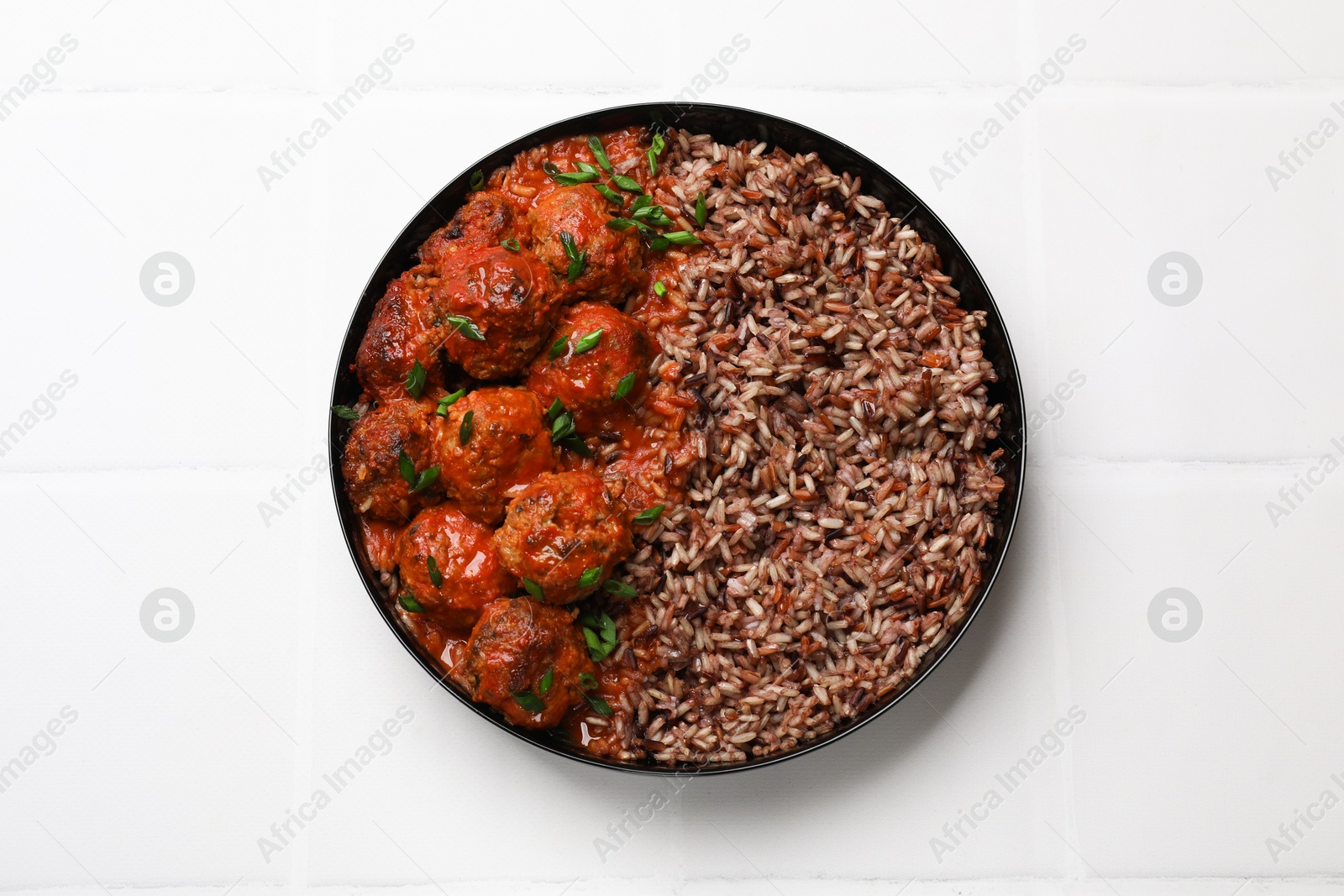 Photo of Tasty meatballs with sauce and brown rice on white tiled table, top view