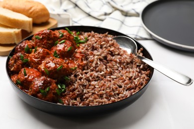 Photo of Tasty meatballs with sauce and brown rice on white tiled table, closeup