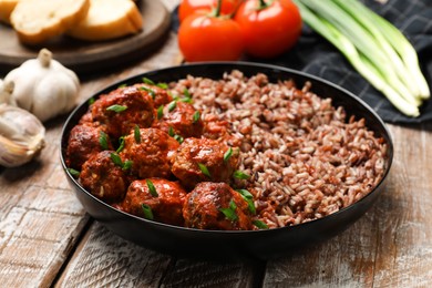 Photo of Tasty meatballs with sauce, brown rice and products on wooden table, closeup