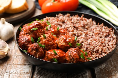 Photo of Tasty meatballs with sauce, brown rice and products on wooden table, closeup