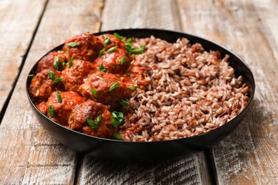 Photo of Tasty meatballs with sauce and brown rice on wooden table, closeup