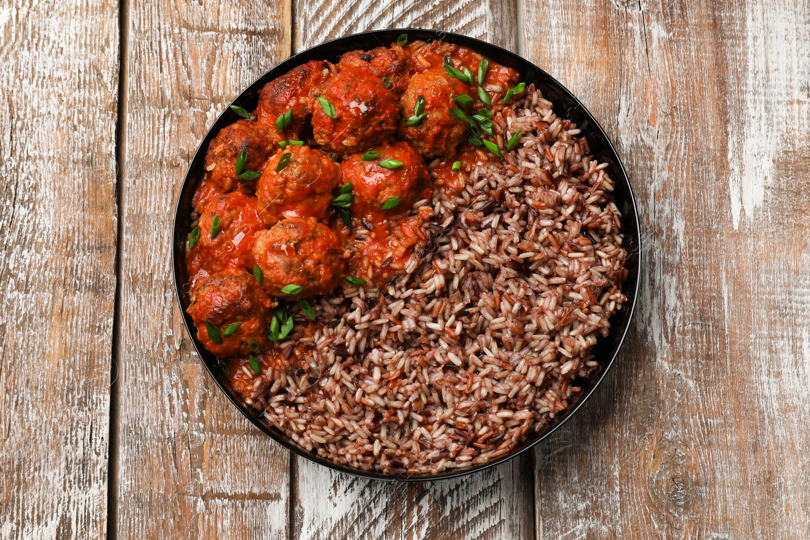 Photo of Tasty meatballs with sauce and brown rice on wooden table, top view