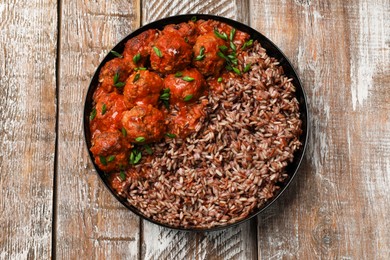 Photo of Tasty meatballs with sauce and brown rice on wooden table, top view