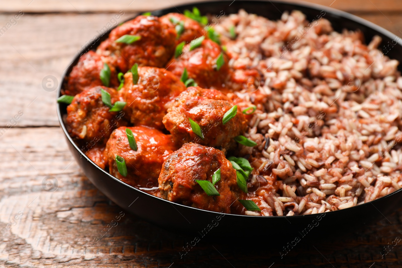 Photo of Tasty meatballs with sauce and brown rice on wooden table, closeup