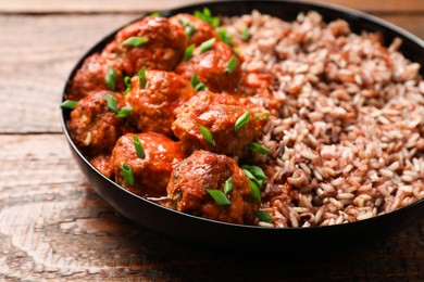 Photo of Tasty meatballs with sauce and brown rice on wooden table, closeup