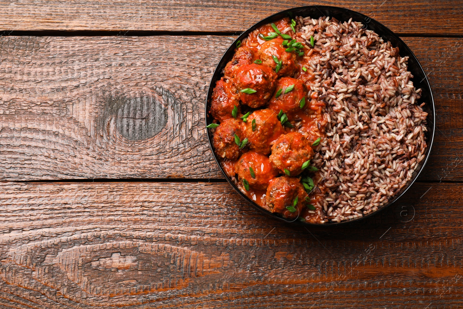 Photo of Tasty meatballs with sauce and brown rice on wooden table, top view. Space for text