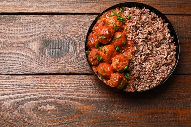 Photo of Tasty meatballs with sauce and brown rice on wooden table, top view. Space for text