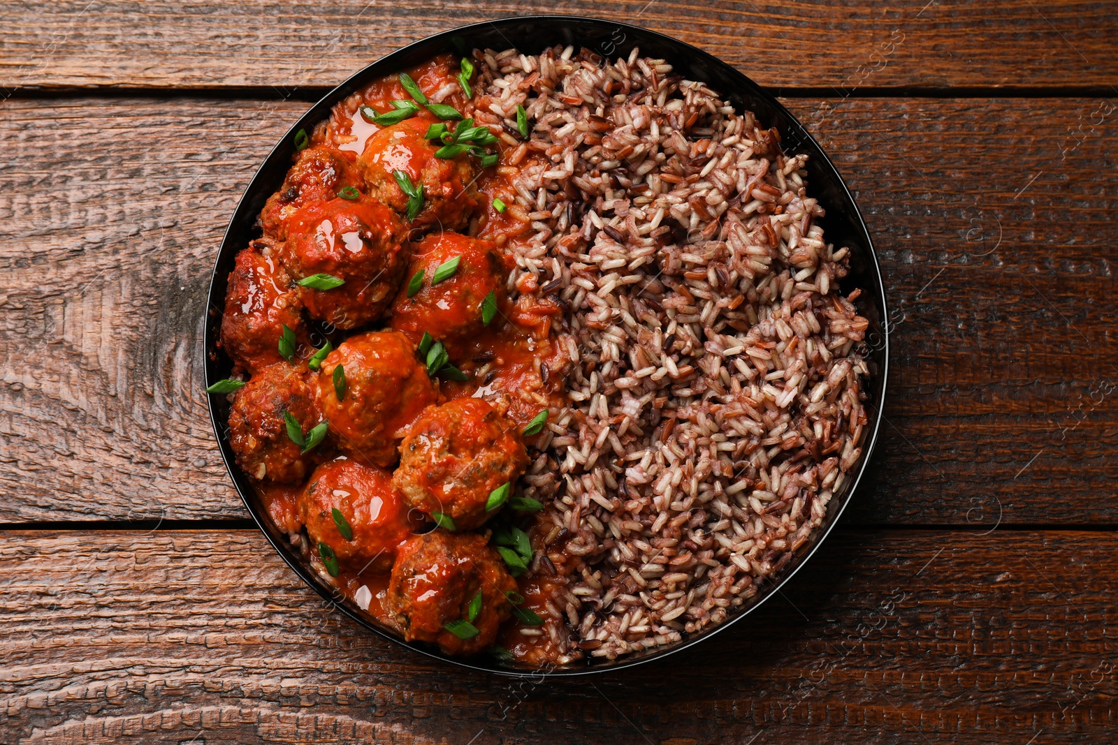 Photo of Tasty meatballs with sauce and brown rice on wooden table, top view