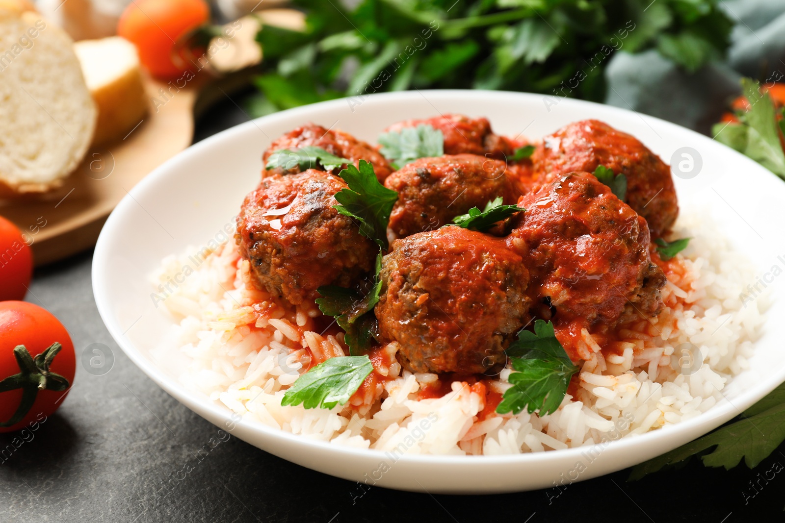 Photo of Tasty meatballs with sauce, rice and products on black table, closeup