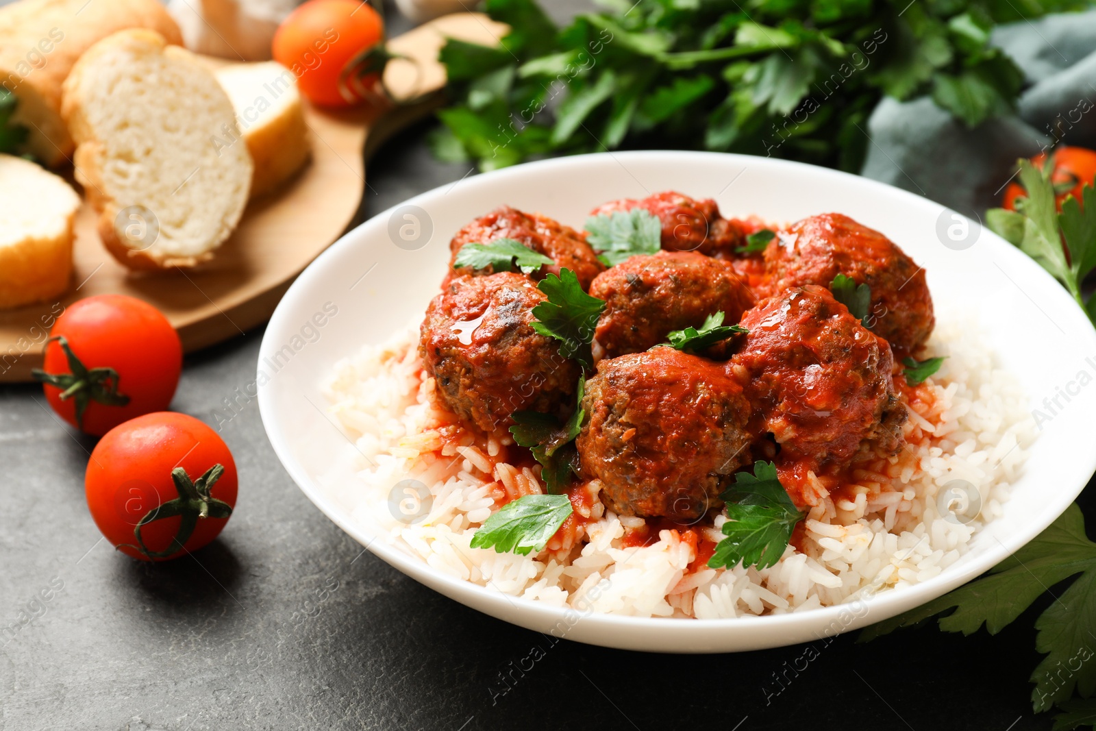 Photo of Tasty meatballs with sauce, rice and products on black table, closeup