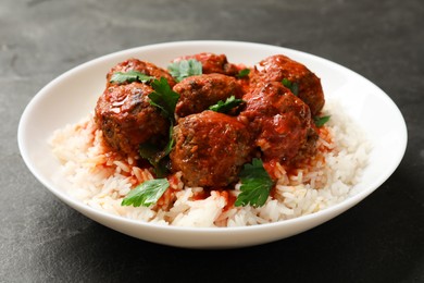 Photo of Tasty meatballs with sauce and rice on black table, closeup