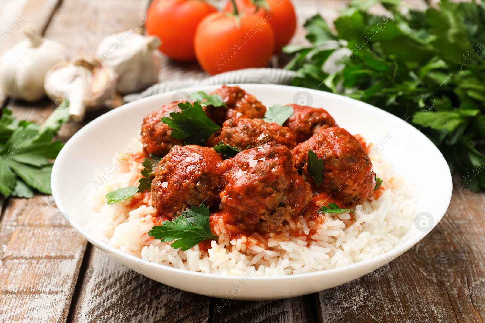 Photo of Tasty meatballs with sauce, rice and products on wooden table, closeup