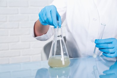 Photo of Laboratory testing. Scientist taking sample from flask at table indoors, closeup. Space for text