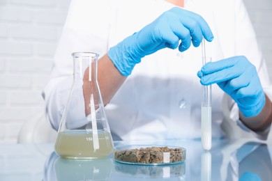 Photo of Laboratory testing. Scientist holding test tube with sample at table indoors, closeup