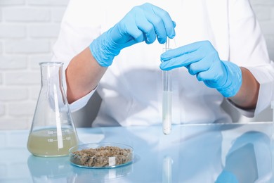 Photo of Laboratory testing. Scientist holding test tube with sample at table indoors, closeup