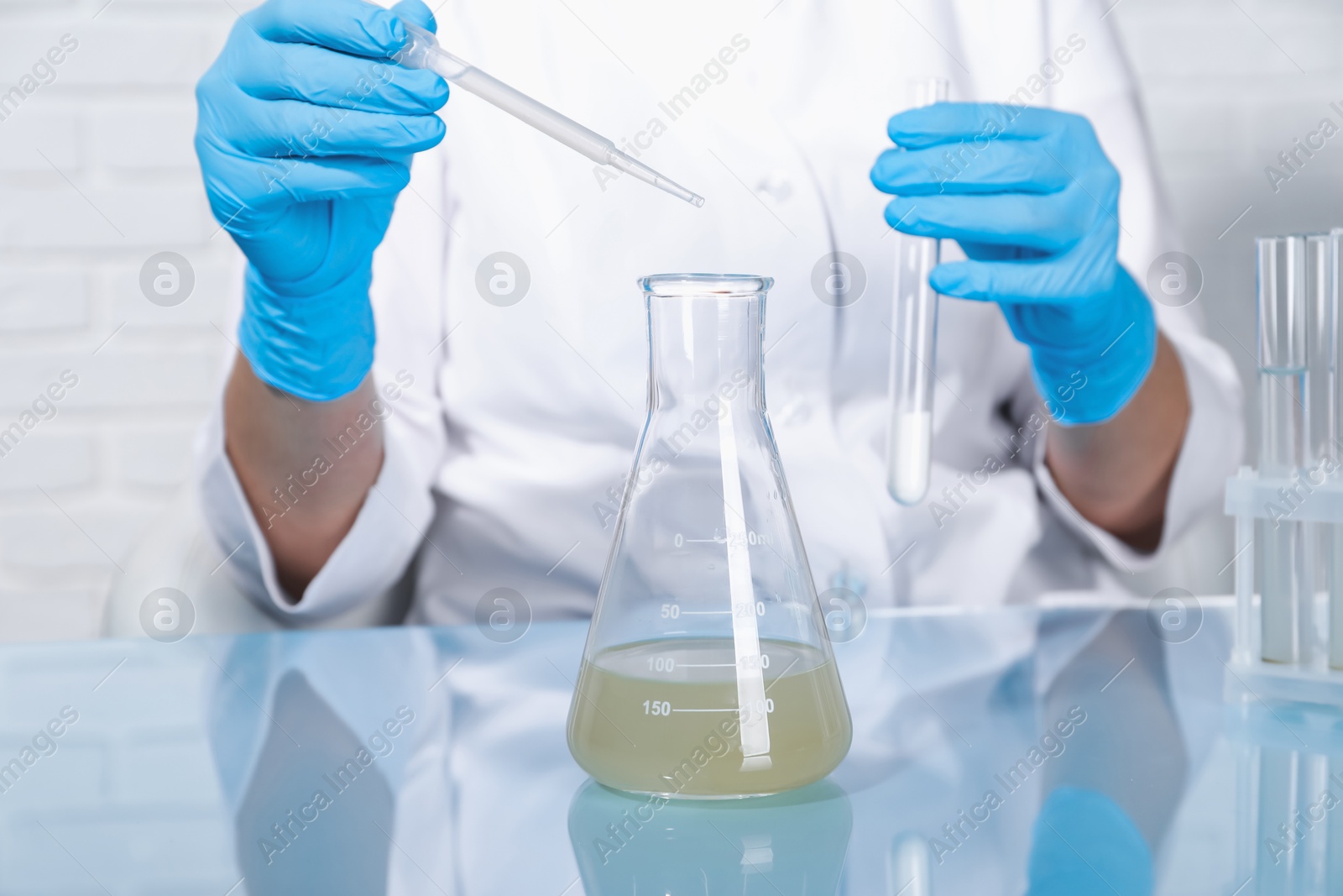 Photo of Laboratory testing. Scientist dripping sample from pipette into flask at table indoors, closeup