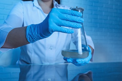 Photo of Laboratory testing. Scientist holding flask with sample at table indoors, closeup