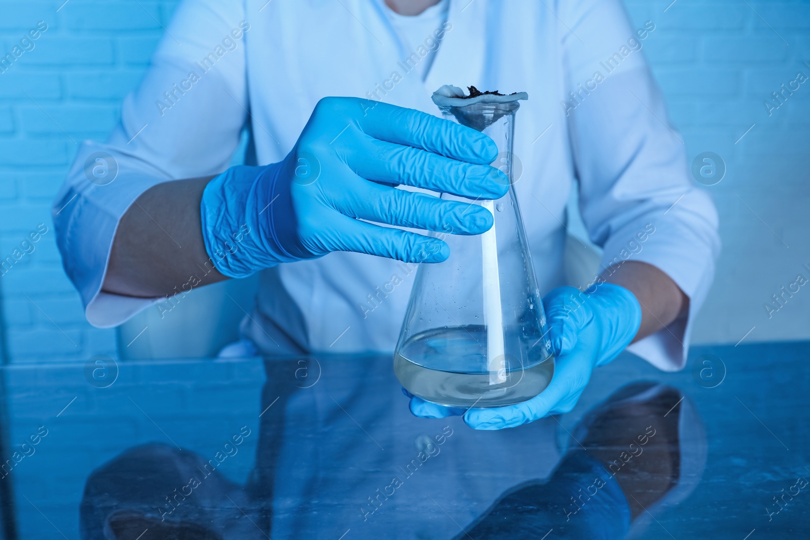 Photo of Laboratory testing. Scientist holding flask with sample at table indoors, closeup