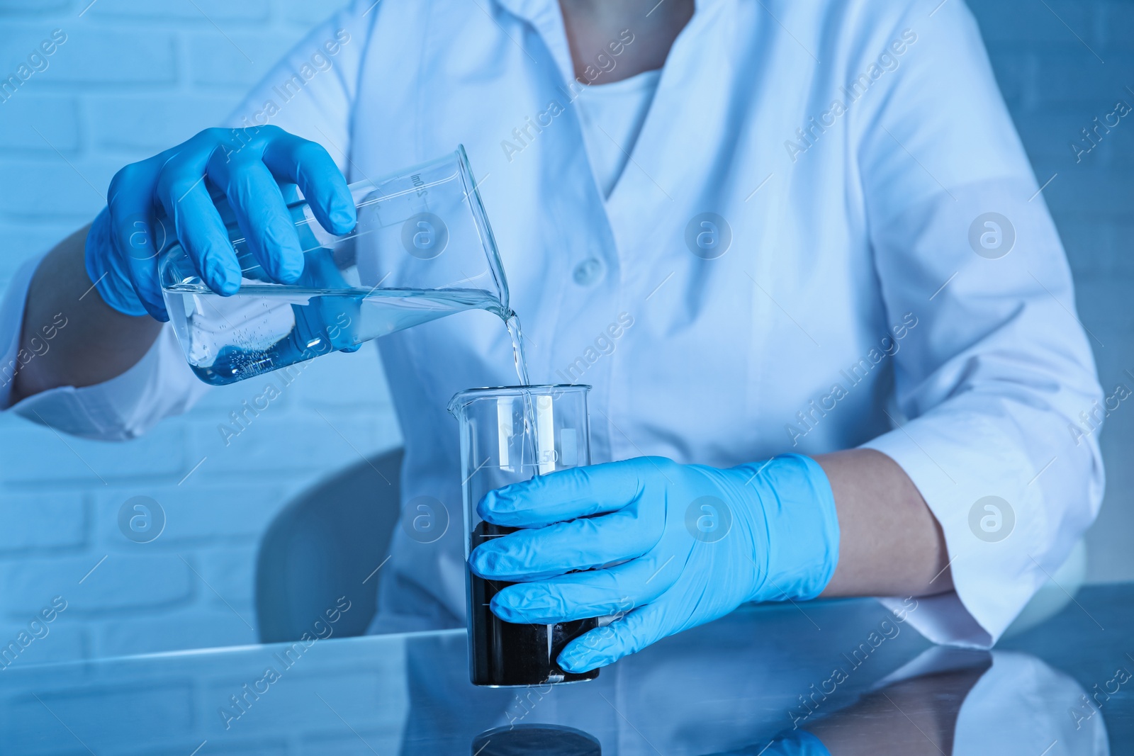 Photo of Laboratory testing. Scientist pouring liquid into beaker at table indoors, closeup