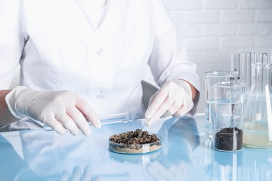 Photo of Laboratory testing. Scientist pouring liquid onto sand sample at table indoors, closeup