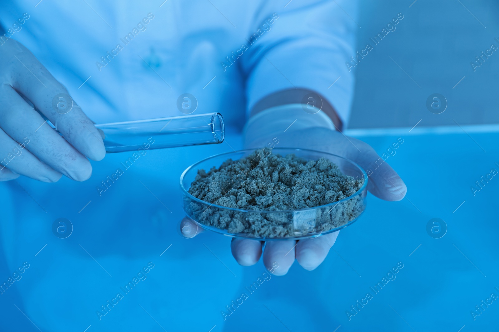 Photo of Laboratory testing. Scientist pouring liquid onto sand sample at table indoors, closeup